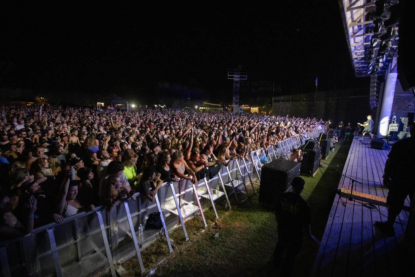 A large crowd at an outdoor concert enjoying a live performance under night sky lighting.