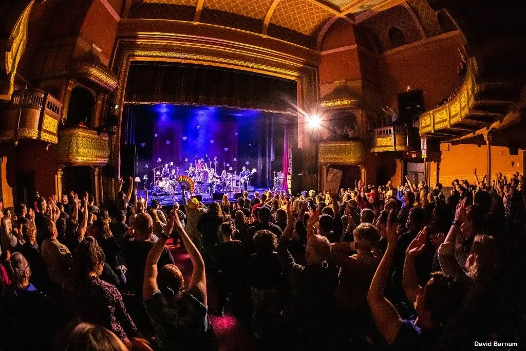 A packed concert audience at a historic venue, watching a live performance on stage, bathed in vibrant lights. Photo credit: David Barnum.