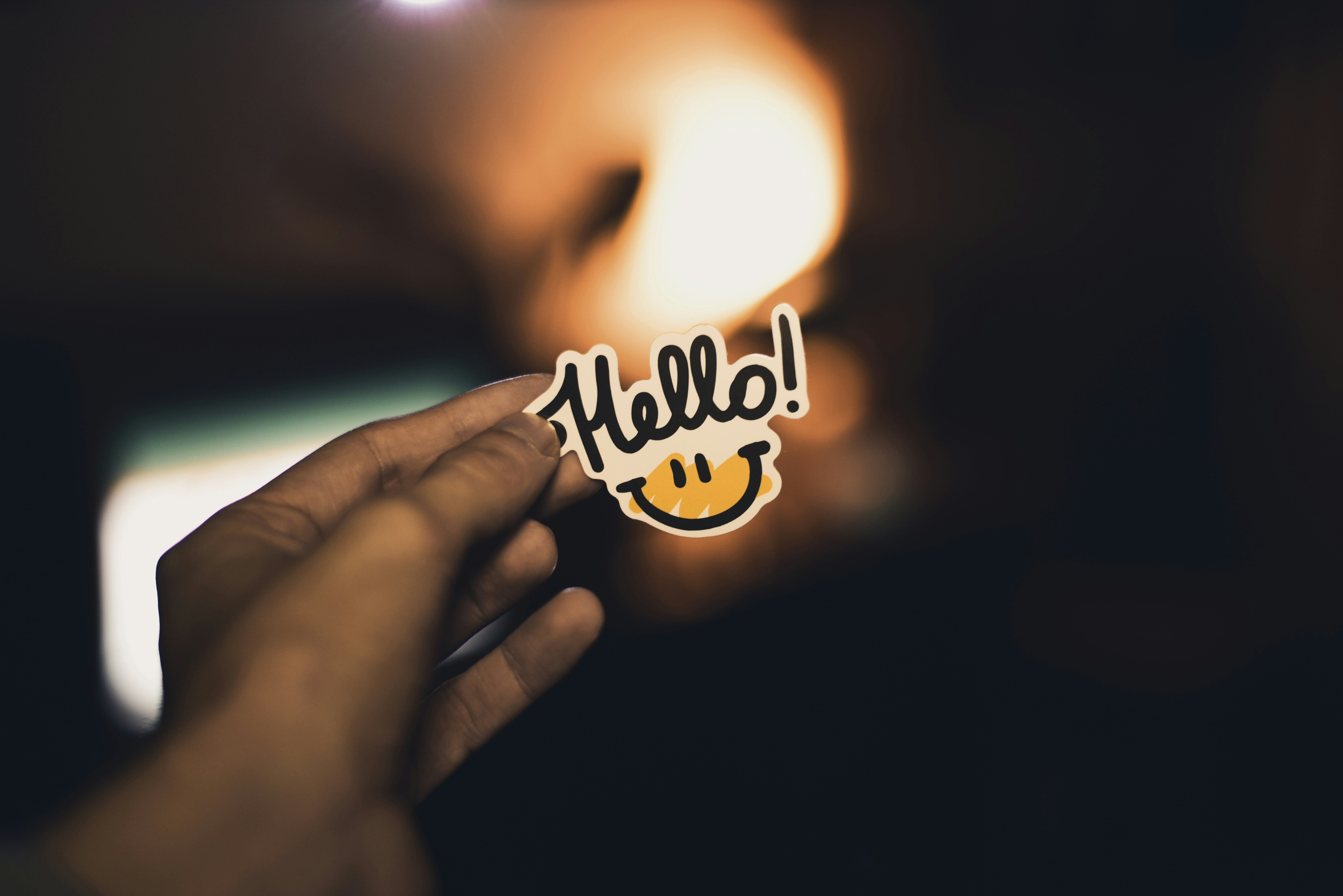 Close-up of a hand holding a sticker with the word 'Hello!' and a smiley face